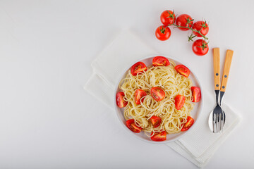 Spaghetti with cherry tomatoes and cutlery on a white background. Spaghetti pasta and red tomatoes on a white napkin. Top view. Copy space