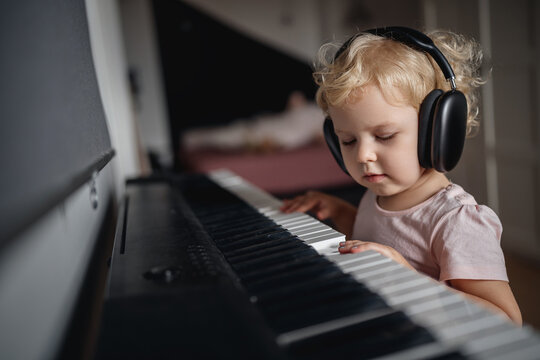 Child girl 4-5 years old in headphones plays music on the keyboard at home. Education and music concept.
