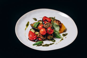 Grilled vegetables on a white plate, isolated on a black background.