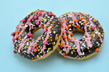two glazed donuts with pink sprinkles on a blue background
