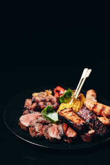 Meat on a black plate. Fried chicken breasts, pork ribs, grilled vegetables, veal. Appetizer for beer with sauces.