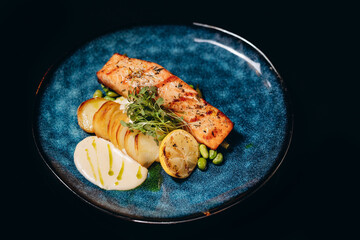 Fried salmon fillet with fried potatoes, lime and vegetable salad served on black plate on wooden table