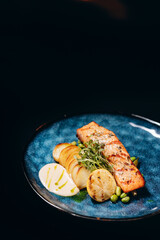 Fried salmon fillet with fried potatoes, lime and vegetable salad served on black plate on wooden table