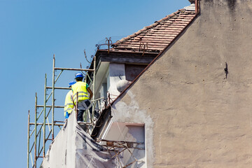 Two unrecognizable construction workers sitting on a scaffolding on a site for house restoration or repairs