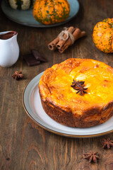 Round cottage cheese casserole with pumpkin layer on a ceramic plate on a brown wooden background. Pumpkin recipes. Thanksgiving, Halloween
