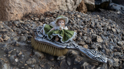 A little ceramic doll and  an old silver comb on the rock. Vintage composition. 
