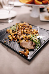 Slice of meat sprinkled with hazelnuts and pine nuts on black stone board