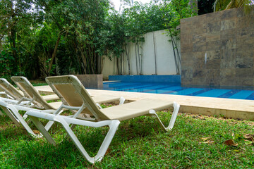 Pool, blue water. Sunbeds on the green lawn. Landscaped garden with swimming pool and sun loungers.