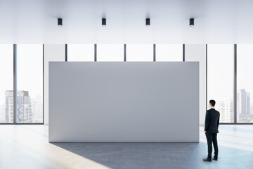 Businessman perspective view looking at big blank white partition with place for advertisement or...