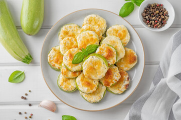 Baked zucchini with cheese, garlic and fresh herbs on a white wooden background. Selective focus