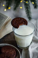 Norwegian Christmas spiced cookies pepperkaker with glass of milk and open book on wooden table and Christmas lights on background 