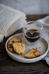 Glass of espresso coffee and homemade biscottis on plate  and open book on wooden table.