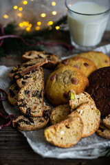 Mix of different kinds of Christmas cookies: biscotti, American chocolate cookies and nordic spicy gingerbread cookies  on baking paper and glass of milk on wooden table.