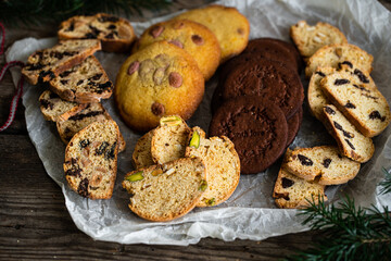 Mix of different kinds of Christmas cookies: biscotti, American chocolate cookies and nordic spicy gingerbread cookies  on baking paper on wooden table.