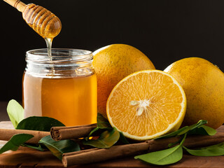 Miel de abeja con naranjas y canela en una tabla de madera. - obrazy, fototapety, plakaty