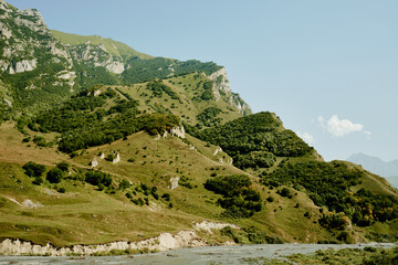 Fototapeta na wymiar Mountain slope with forests, meadows and river at foot on sunny day. North Ossetia-Alania, Russia.