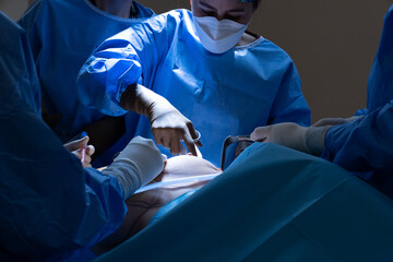 Surgeon and his assistant performing cosmetic surgery in hospital operating room. Surgeon in mask wearing loupes during medical procadure. Breast augmentation, enlargement, enhancement, breast cancer