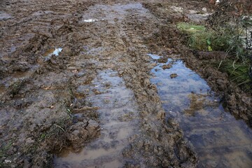 Braune Schlammlandschaft mit Fahrspurrillenmuster und großen Wasserpfützen am Morgen im Winter