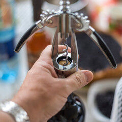 man's hand opens a bottle of wine with a corkscrew