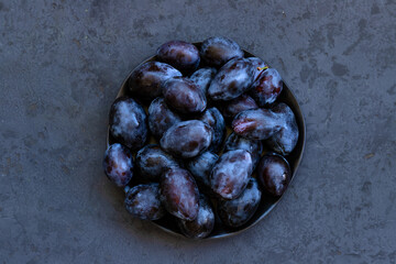 Fresh ripe blue plums on plate on dark gray background. Low key photo. Top down view. Close-up. Flat lay composition. Copy space.