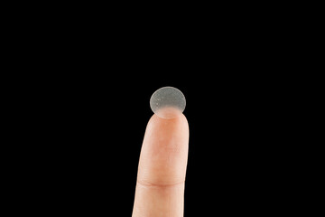 Close-up round acne patch on finger on black background. Acne patches for treatment of pimple and...