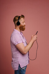Adult stylish redhead bearded calm man in headphones with phone