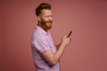 Adult stylish handsome redhead bearded smiling winking man holding phone