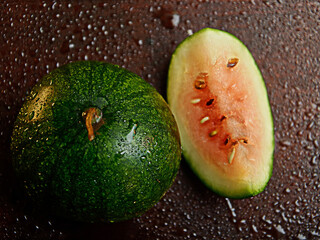 watermelon whole and a piece on a dark wooden background with water drops