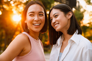 Two asian women laughing and talking during meeting in park