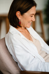 White mature woman in shirt smiling while sitting in cafe indoors