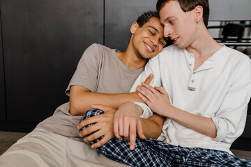 Happy young multiracial gay couple smiling and hugging together at home