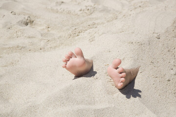 Child feet buried in the sand on the beach	