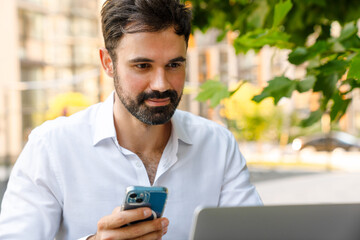 White bearded man using cellphone and laptop while sitting at table