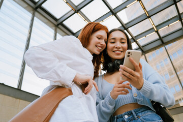 Young multinational women smiling and using cellphone indoors