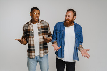 Two multinational displeased men gesturing while looking at each other isolated