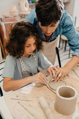 Mature woman teaching boy to make clay crafts at workshop