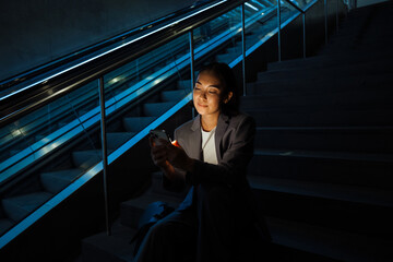 Asian woman using mobile phone while sitting on the stairs next to escalator - Powered by Adobe