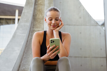 Young beautiful smiling sporty woman holding and using her phone