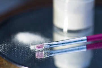 White acrylic powder to strengthen the nail plate and a brush in the reflection of the mirror