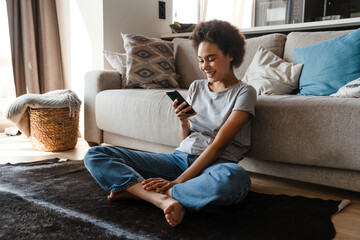 Obraz premium Young beautiful smiling curly african woman holding and using phone