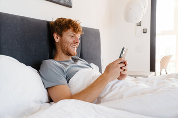 Young handsome smiling redhead man in gray t-shirt with phone