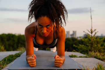 Young beautiful serious tense curly african woman holding plank position