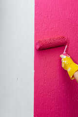 A girl paints a wall close-up with a roller in pink in her new apartment. Renovation of the interior and a new apartment. Housewarming and a desirable mortgage.