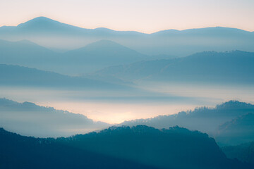 A blue and orange glowing view of layers of mountains in the Smoky Mountains in North Carolina. There is a lot of haze and fog in the mountain valleys. 