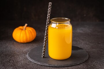 Pumpkin juice with ice in a transparent glass glass on a black slate stand on a black concrete background. Vegetable juices. Thanksgiving, Halloween