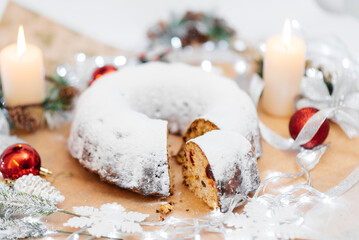 Traditional round Christmas stollen made of dried fruits and nuts, sprinkled with powdered sugar on the background of a Christmas decor with candles. A festive treat.