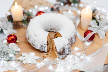 Traditional round Christmas stollen made of dried fruits and nuts, sprinkled with powdered sugar on the background of a Christmas decor with candles. A festive treat.