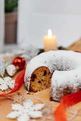 Traditional round Christmas stollen made of dried fruits and nuts, sprinkled with powdered sugar on the background of a Christmas decor with candles. A festive treat.