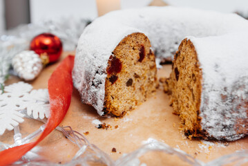 Traditional round Christmas stollen made of dried fruits and nuts, sprinkled with powdered sugar on the background of a Christmas decor with candles. A festive treat.