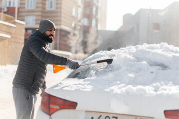 A young man cleans his car after a snowfall on a sunny, frosty day. Cleaning and clearing the car...